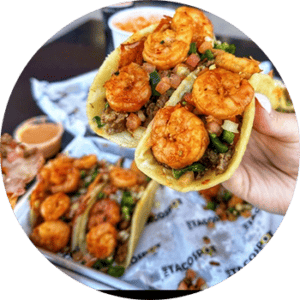 A hand holding a taco with shrimp on it.