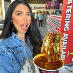 A woman holding up a bowl of tacos in a restaurant.